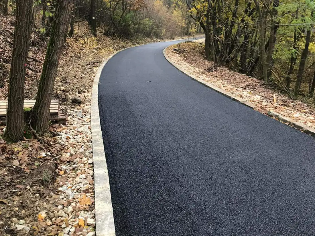 Kanyarodó aszfaltozott gyalogút erdőszélen, betonszegéllyel és zúzottkő padkával