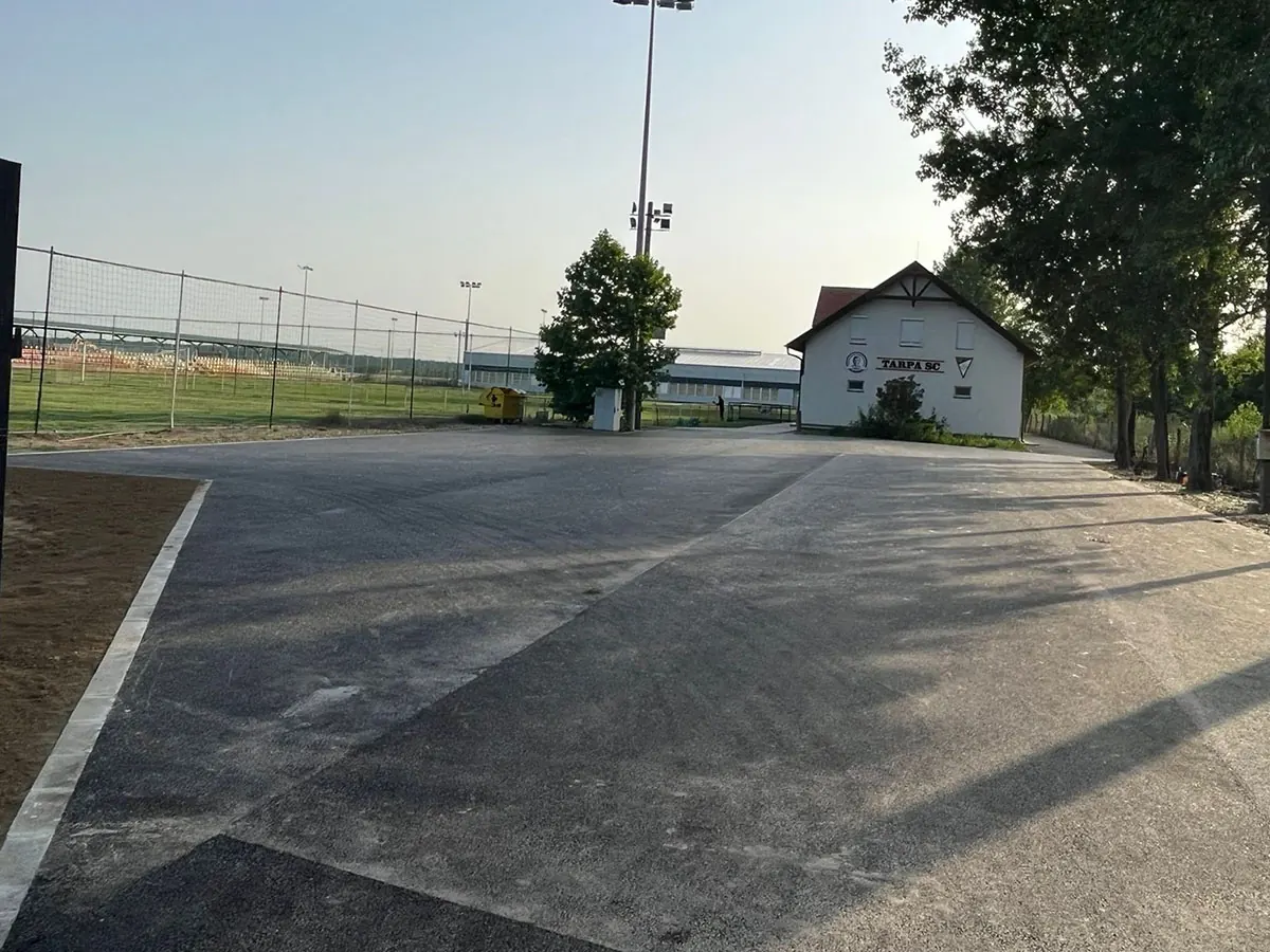 Frissen aszfaltozott parkoló sportpálya és épület mellett, reflektoroszlopokkal