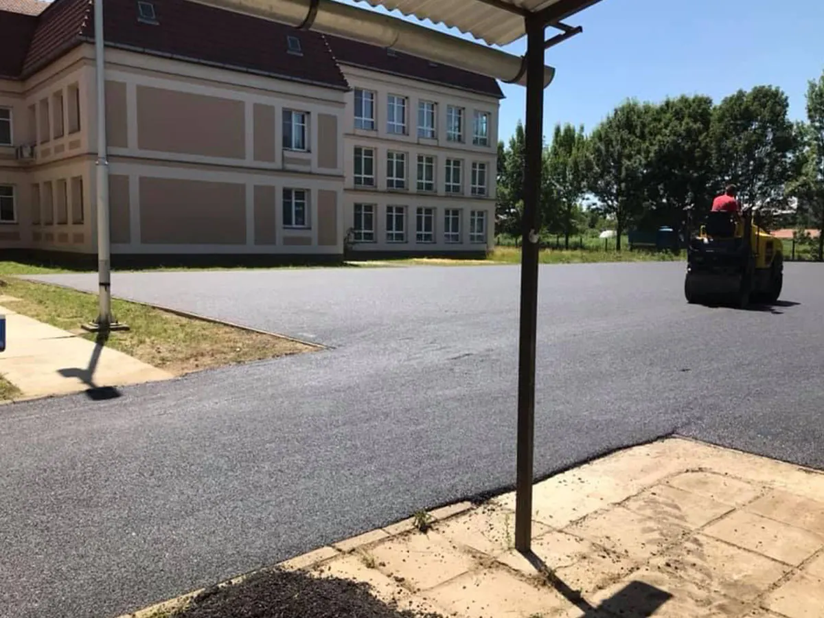 Iskolaépület előtti udvar és parkoló aszfaltozása, henger tömöríti a friss réteget
