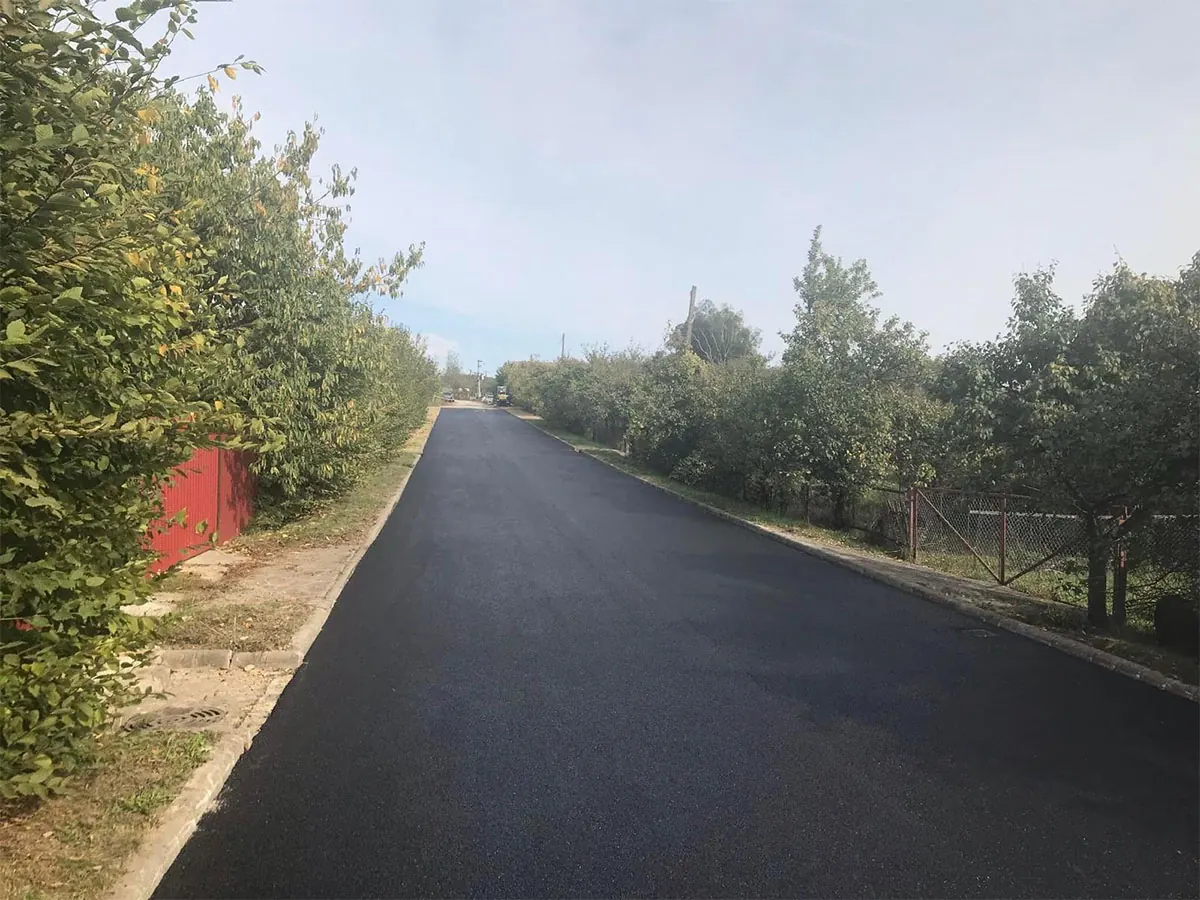 Aszfaltozott út lakóövezetben, fák és sövény között